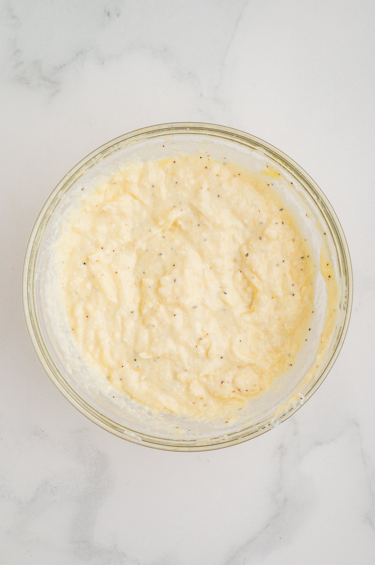 Overhead shot of the cheese filling after mixing—creamy ricotta blended with egg, mozzarella, Parmesan, salt, and pepper in a glass bowl.