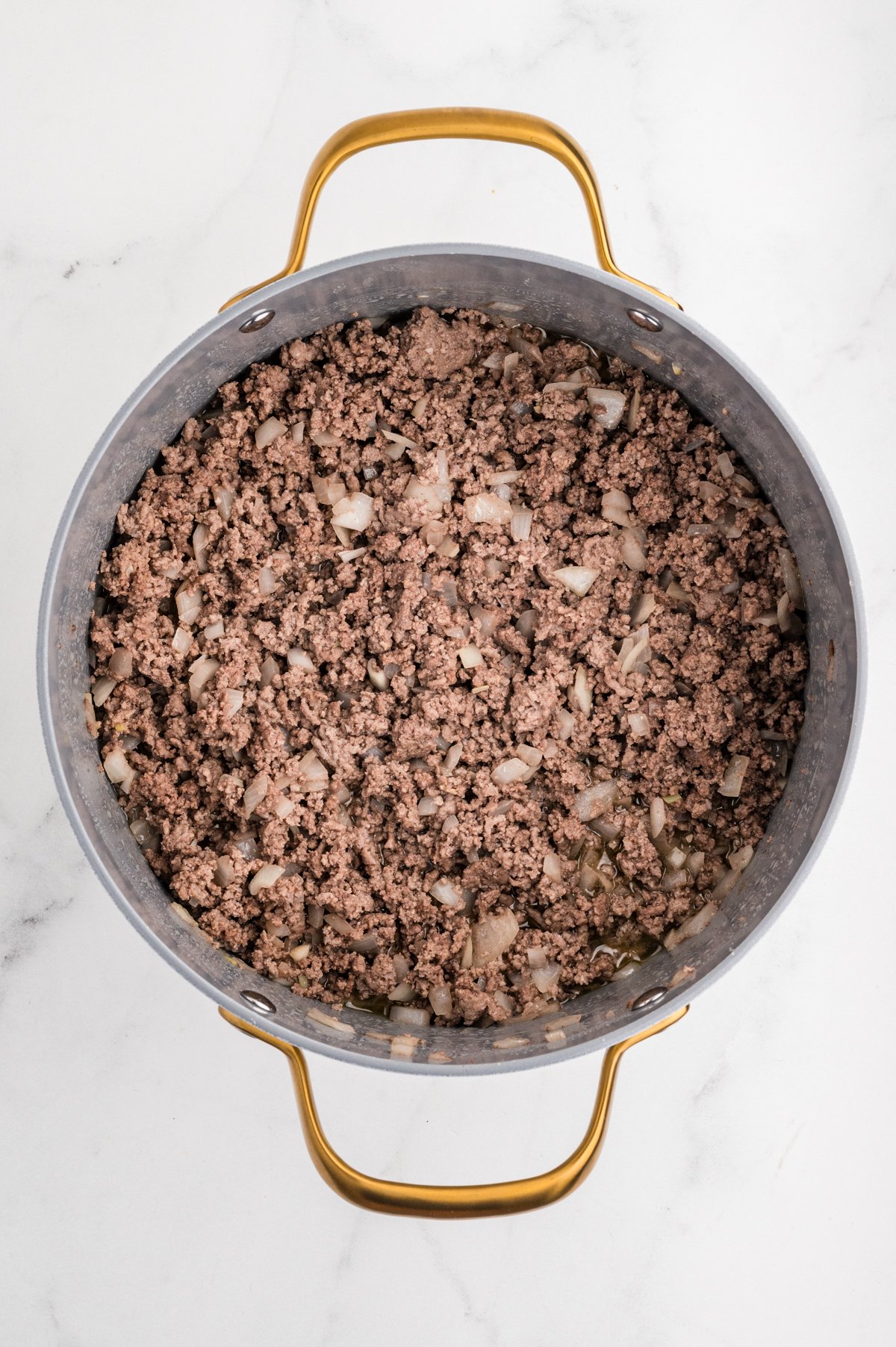 Top-down view of a large skillet containing cooked ground beef and white onion over a white countertop.