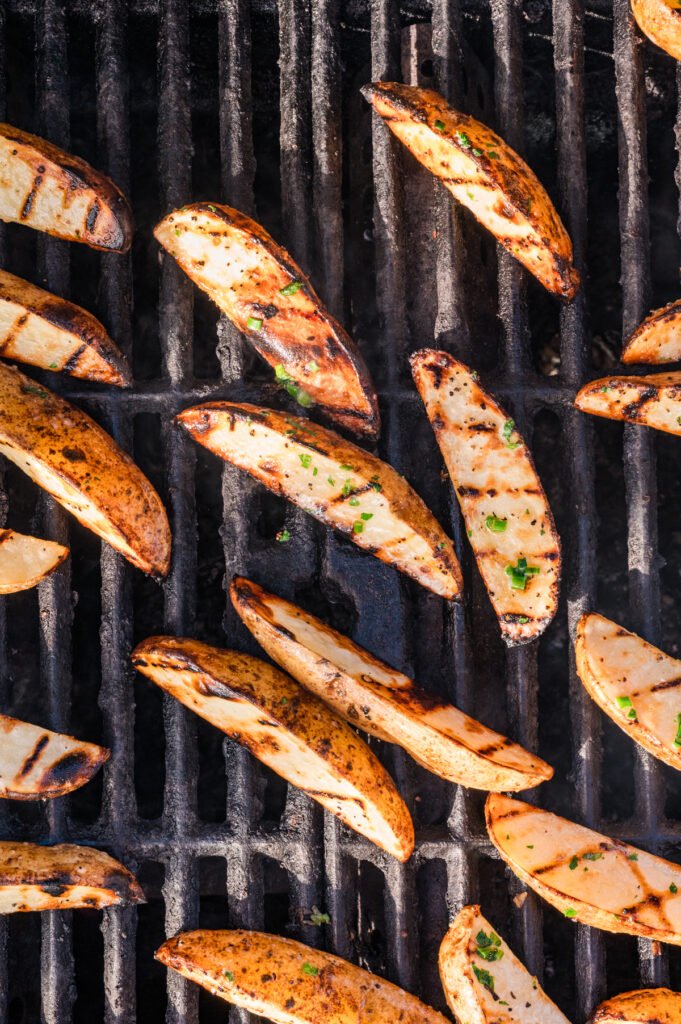 Top-down view of fully grilled potato wedges lying on grill grates, showing dark grill marks, a golden-brown exterior.