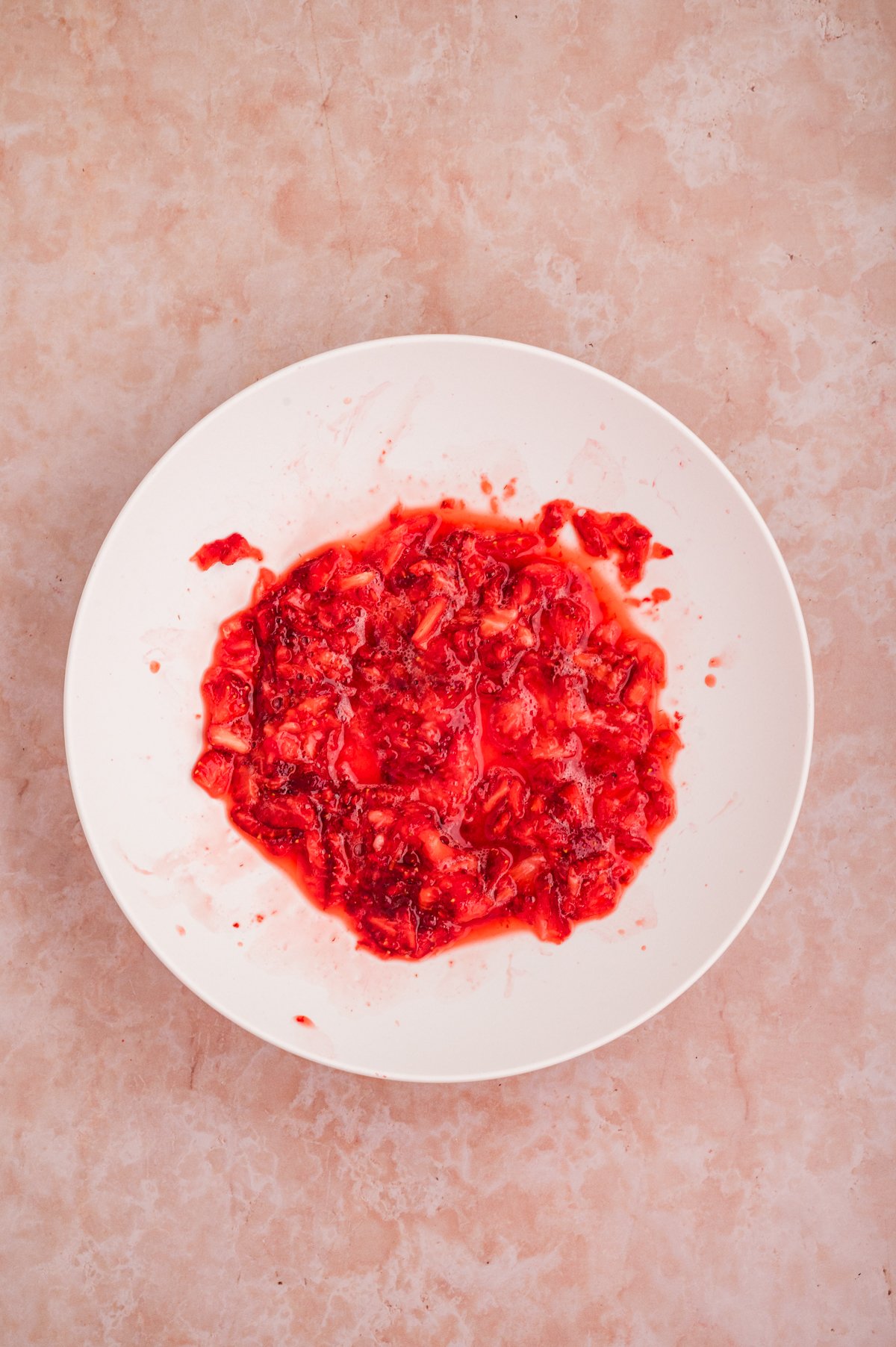 Strawberry butter in a white bowl shows mashed strawberries.