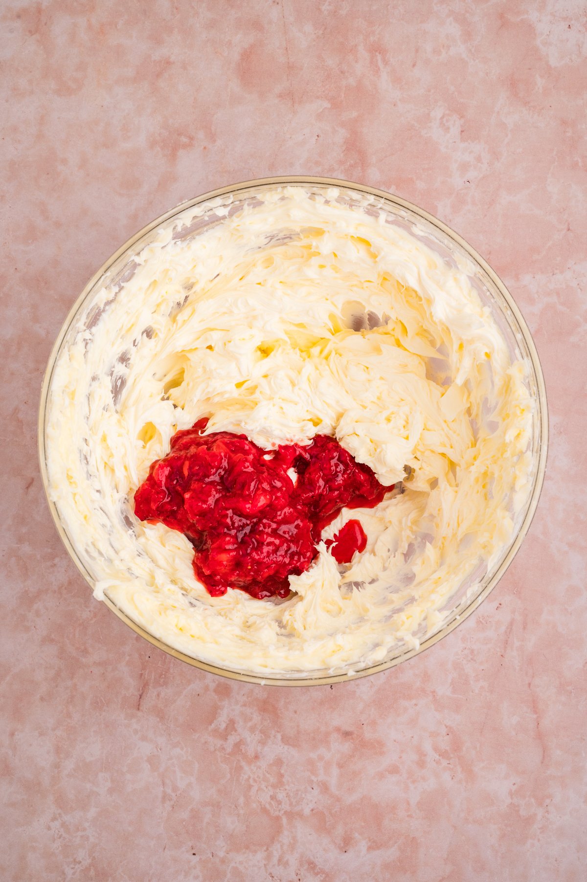 Strawberry butter ingredients sit in a glass mixing bowl: whipped butter around a pile of mashed strawberries.