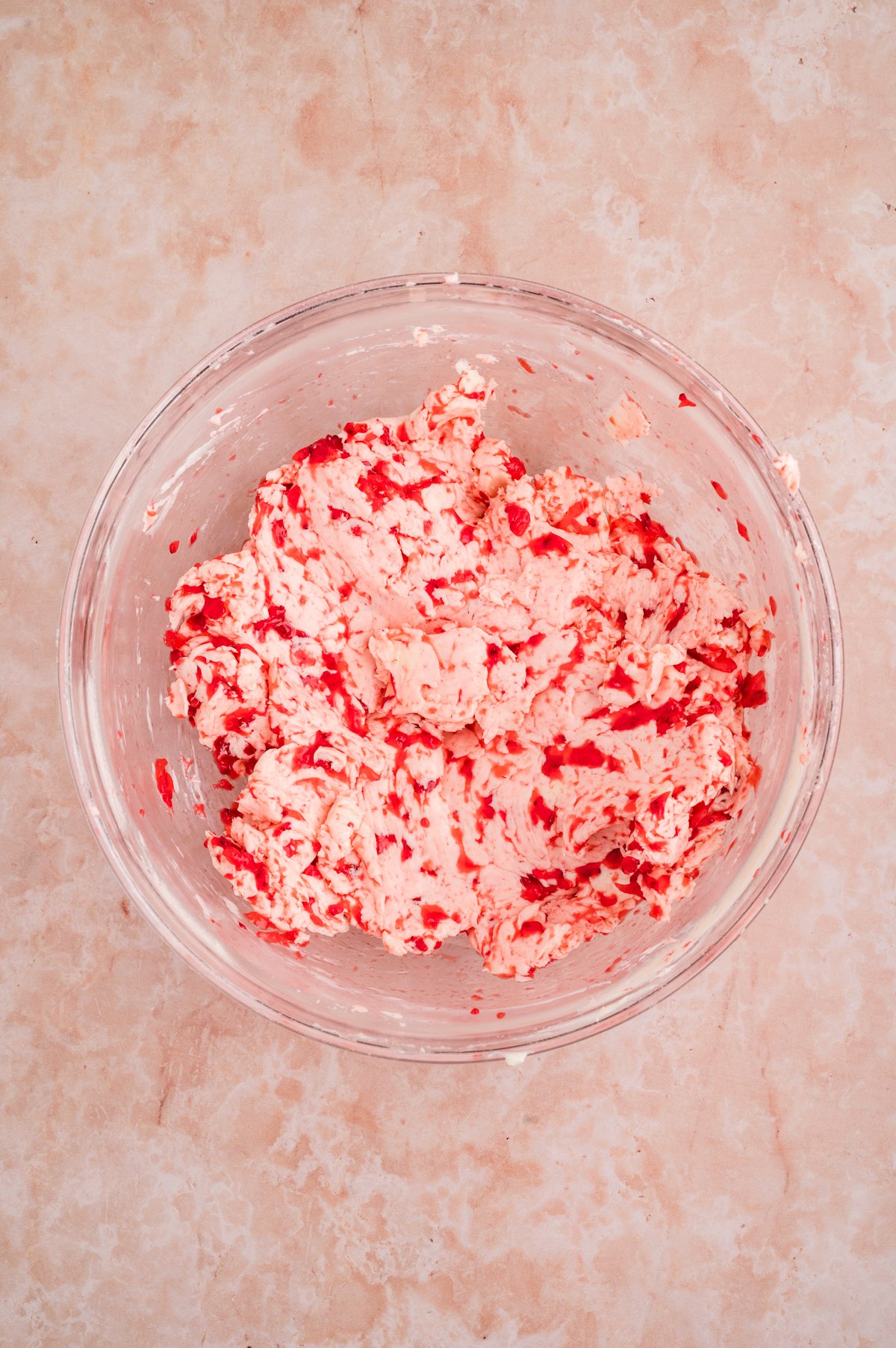 A clear glass bowl showing whipped pale butter mixed with mashed strawberries.