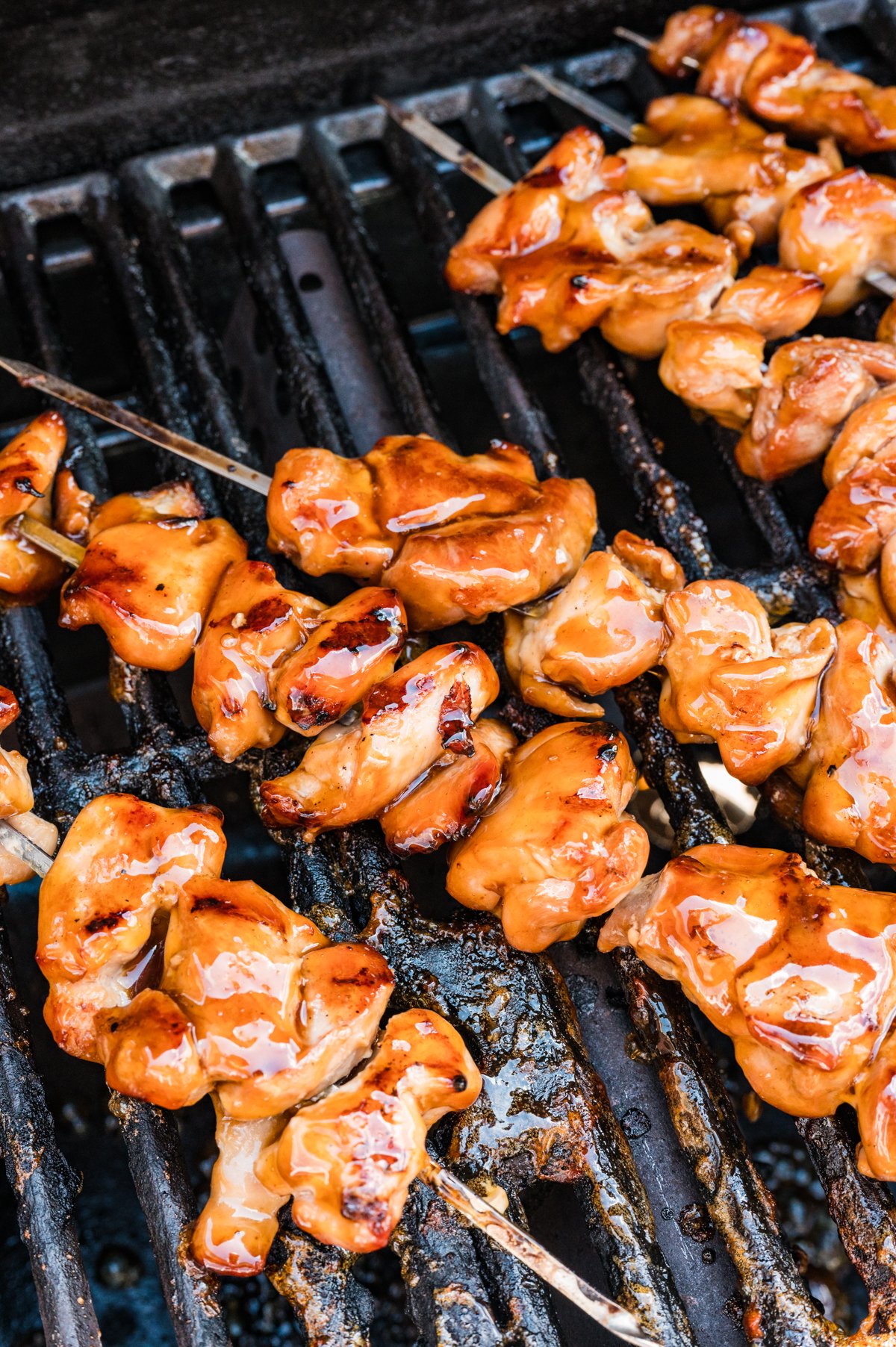 Close-up of golden-glazed chicken skewers finishing cooking on a hot grate.