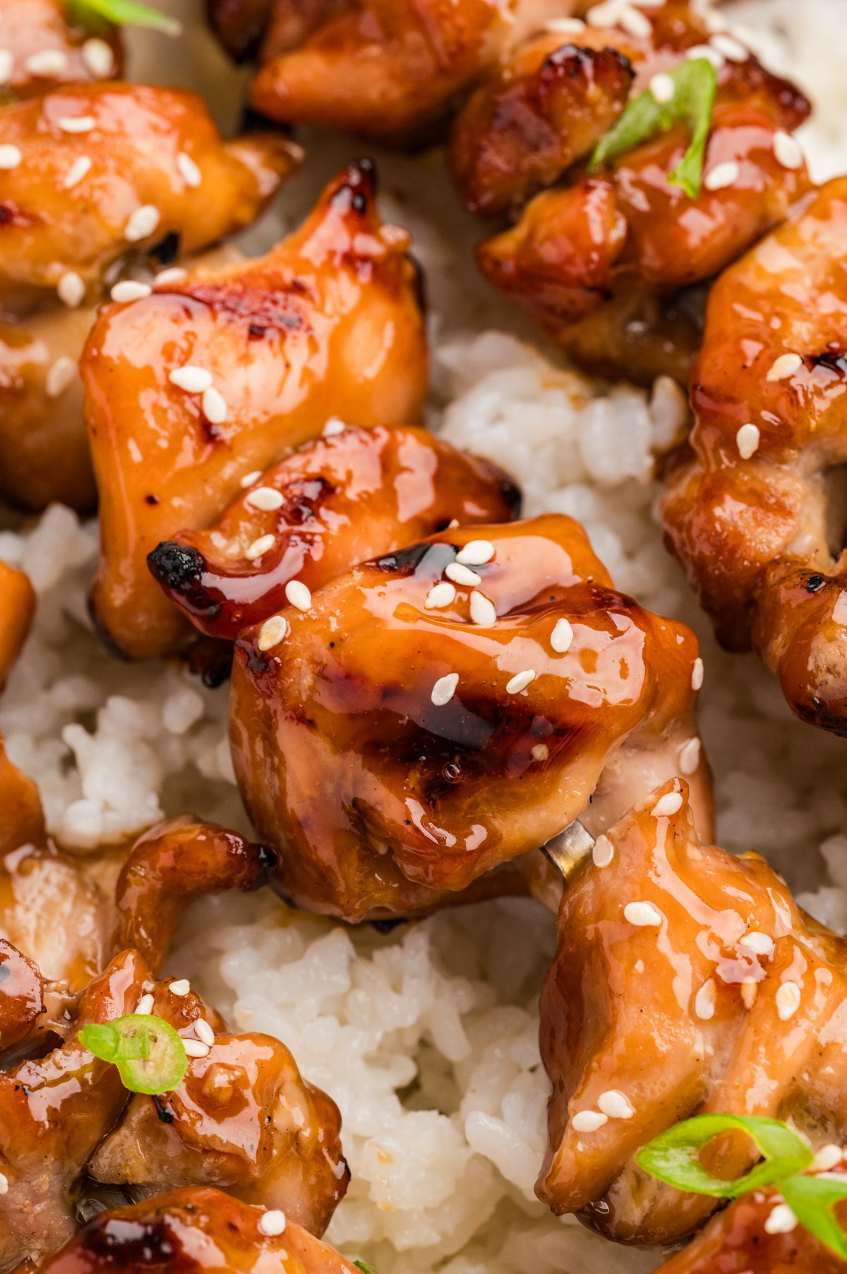 Glazed teriyaki chicken skewers nestled atop a bed of steamed white rice, sprinkled with sesame seeds.