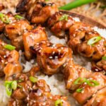 Overhead view of three teriyaki chicken skewers served on rice, garnished with sliced green onions and sesame seeds.