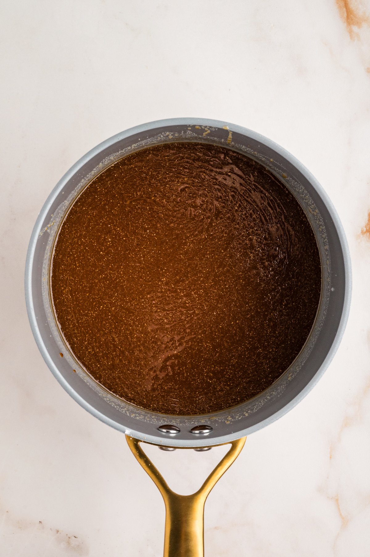 Saucepan on the counter with light brown teriyaki sauce beginning to bubble and thicken.