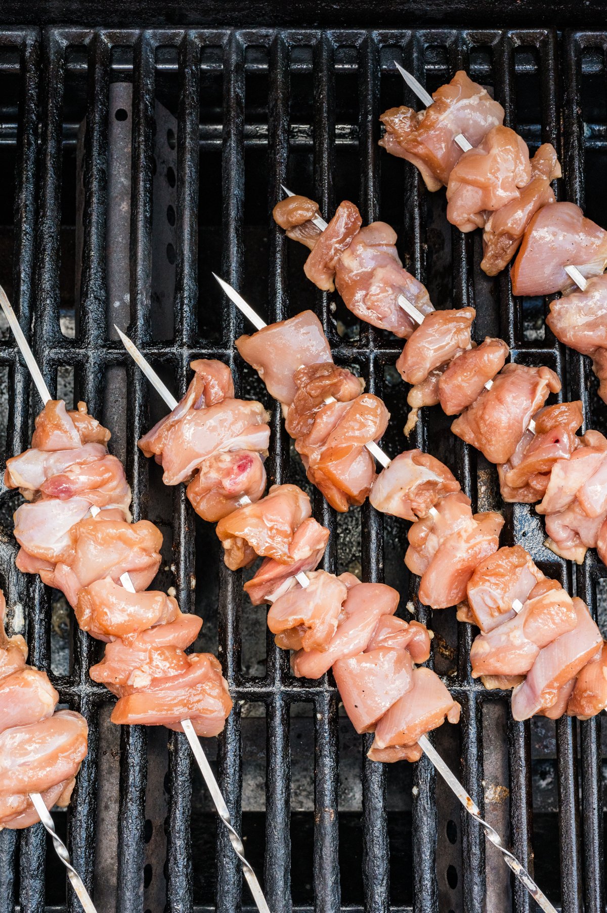 Raw chicken-topped skewers placed directly on a hot grill grate for cooking.