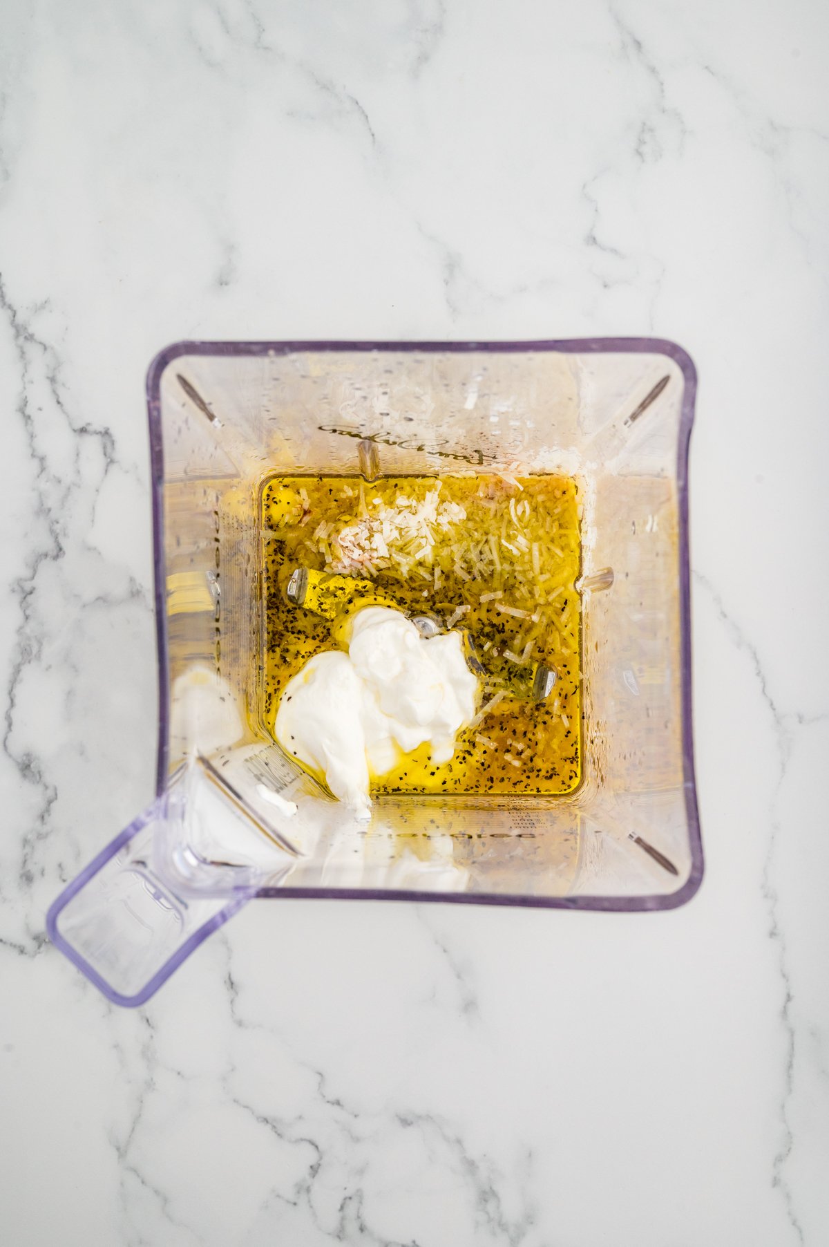 Ingredients for homemade Caesar dressing in a blender including olive oil, Greek yogurt, and shredded parmesan cheese