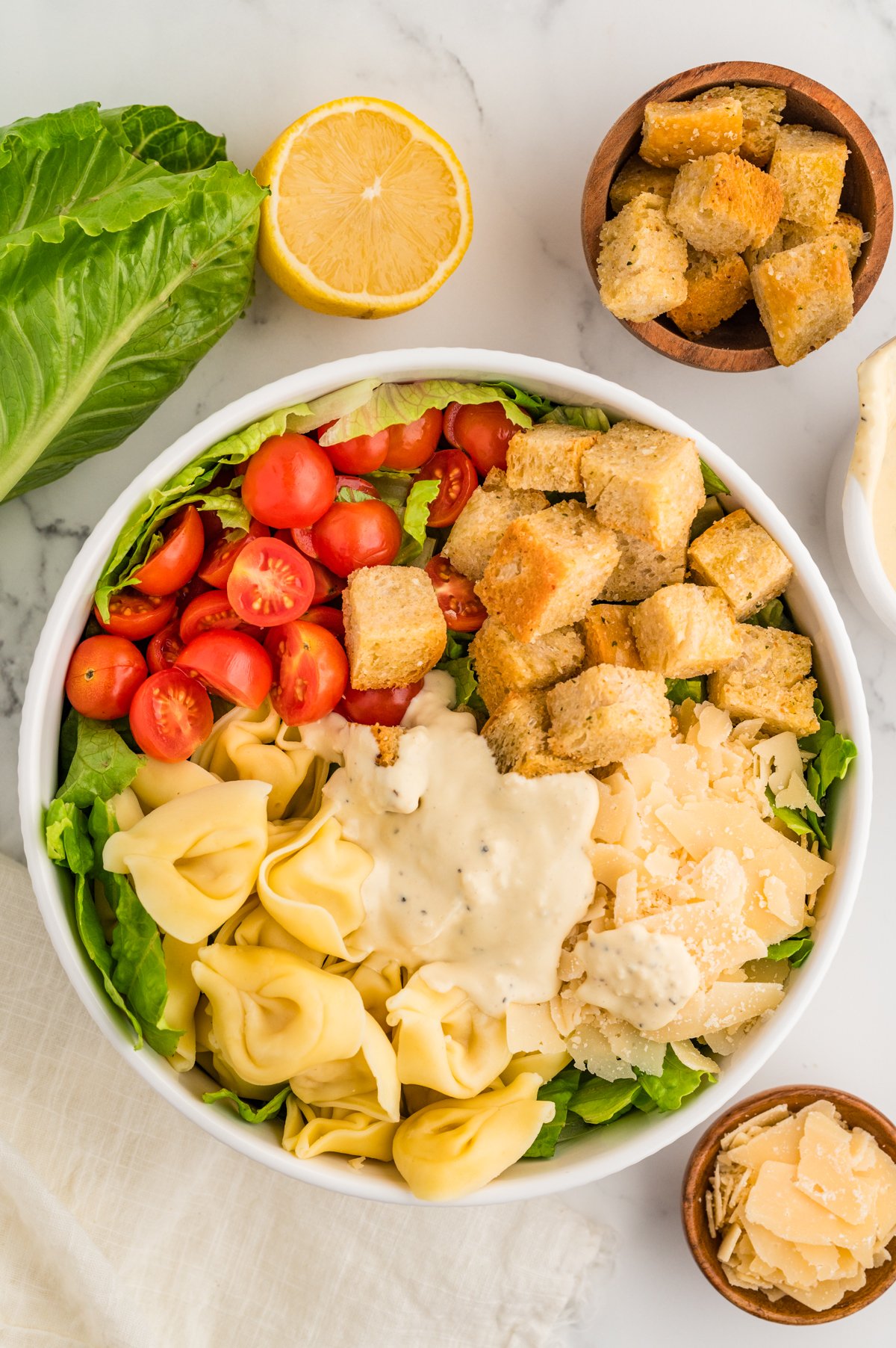 Unmixed tortellini Caesar salad in a bowl with romaine lettuce, cherry tomatoes, croutons, shaved parmesan, and dressing